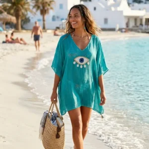 Kvinna i turkos kaftan med stort öga i guld och vitt på strand