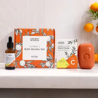 Produktpaket med Vitamin C-serum, badbomber och handtvål på vit hylla med apelsiner i bakgrunden