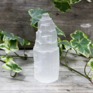 Naturligt selenittorn med mjölkig satinlyster på träyta med gröna blad runtom