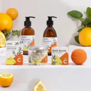 Produktpaket med Vitamin C handtvål, kroppslotion, badbomb och vispad tvål på vit hylla med citrusfrukter runtom